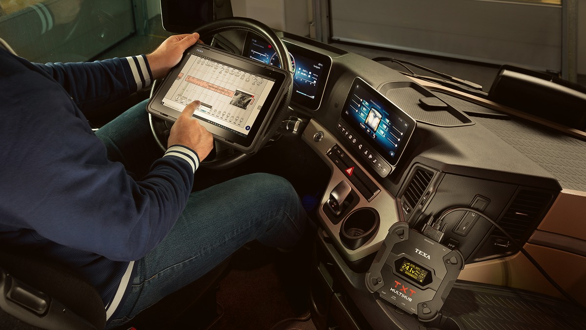 Technician in a truck cab using a TEXA AXONE VOICE tablet to view a wiring diagram, with a TEXA TXT Multihub 2 connected and lit on the dash.